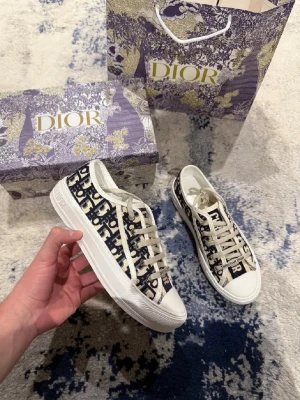 Dior Oblique sneakers med logga - Snygga Dior Oblique sneakers i beige och marinblått tyg med tydlig logotypdesign. Skorna har vita gummisulor, svarta skosnören och detaljer i vitt. Klassisk låg modell med 'Christian Dior' på snörningen. Perfekta för dig som gillar lyxig streetstyle.