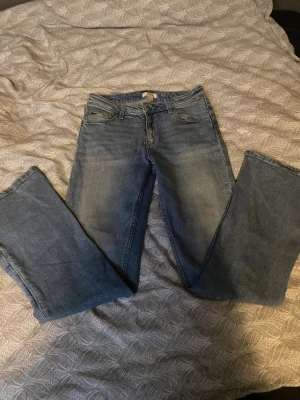 Blå bootcut jeans i klassisk modell - Säljer ett par ljusblå bootcut jeans med fem fickor och normal midja. Jeansen har en klassisk tvätt och raka ben som slutar i en lätt utsvängning. Tillverkade i denim med en skön känsla och passar perfekt till en avslappnad stil.