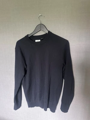Svart stickad tröja H&M Essentials - Klassisk svart stickad tröja från H&M Essentials, modell No 8. Tröjan har rund halsringning, långa ärmar och ribbade muddar vid ärmslut och nederkant. Regular fit och enkel design som passar till det mesta.
