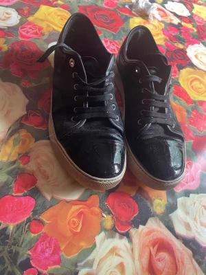 Lanvin - Hej! Jag säljer ett par Lanvins i storlek 43. Med någon liten defekt på lådan och en liten läder bit har lossnat. Snygga svarta sneakers med glansig finish och klassisk vit sula. Skorna har snörning framtill och en stilren design som passar till det mesta. Perfekta för dig som vill ha ett par stilrena och bekväma sneakers till vardagslooken. Pris går att diskuteras😁