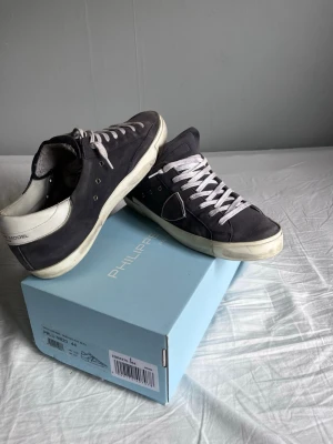 Philippe Model  - Snygga blåa sneakers från Philippe Model med vita detaljer och vita skosnören. Skorna har en klassisk låg silhuett, vit sula och är tillverkade i mocka och läder. Perfekta för dig som gillar stilrena och trendiga sneakers.
