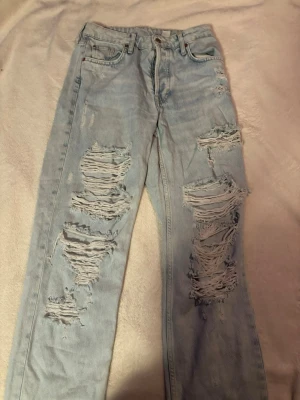 Ljusblå ripped jeans från H&M - Säljer ett par ljusblå jeans från H&M med stora hål på både fram- och baksida. Jeansen har raka ben, klassisk femficksmodell och hög midja. Perfekta för en avslappnad och trendig streetstyle-look.