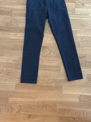 Mörkblå chinos från A Day's March - Snygga mörkblå chinos från A Day's March med rak passform och klassisk design. Tillverkade i ett mjukt bomullstyg som ger en skön känsla och stilren look. Perfekta för dig som vill ha ett par stilrena byxor till garderoben.
