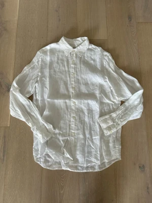 Linneskjorta från Uniqlo - Klassisk vit skjorta från Uniqlo i svalt linne. Skjortan har lång ärm, knappar framtill och en tidlös krage. Perfekt för en clean och stilren look, lätt att matcha med olika outfits.