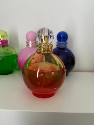 Britney Spears Blissful Fantasy Eau de Toilette 100 ml - Originalparfym. Cirka 65–70 ml kvar i flaskan (se bilder för innehållsnivå). Ingen originalkartong finns kvar. En feminin och somrig doft där saftig melon möter mjuk fresia och lilja. I hjärtat blommar jasmin, tuberos och exotisk tiareblomma från Tahiti, medan basen av irisrot, sandelträ och mysk ger en mjuk, krämig och elegant avslutning. 