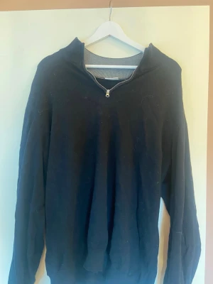 Svart halvzip tröja John Henric - Snygg svart tröja från John Henric med halvzip och hög krage. Tillverkad i mjukt material och har ribbade muddar vid halsen. Perfekt för en stilren och avslappnad look.