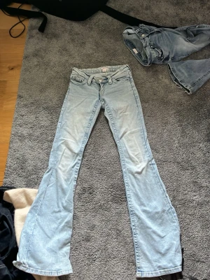 Ljusblå bootcut jeans från Gina tricot  - Säljer ett par ljusblå bootcut jeans från Replay med klassisk femficksmodell och snygga detaljer på bakfickorna. Jeansen har låg midja och är tillverkade i mjuk denim med lite stretch för skön passform. Perfekta för dig som gillar retrovibbar och avslappnad stil.