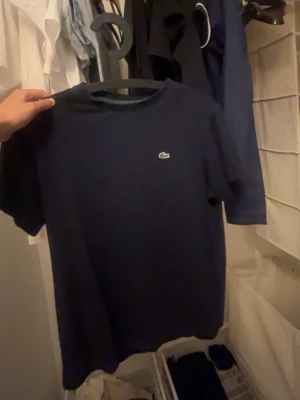 Mörkblå t-shirt från Lacoste - Snygg mörkblå t-shirt från Lacoste med den klassiska krokodilloggan broderad på bröstet. T-shirten har rund halsringning och korta ärmar. Perfekt basplagg med clean look och skön passform.