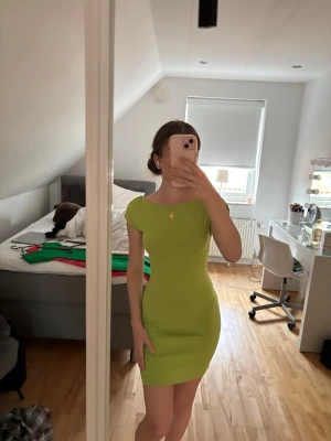Limegrön tight kortklänning - Säljer en limegrön kortklänning med tight passform och öppen rygg. Klänningen har korta ärmar och en enkel, stilren design som framhäver figuren. Perfekt för dig som vill sticka ut med en färgstark look.