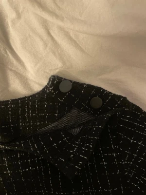 & Other story svart topp - Svart kortärmad topp med vita streck i rutmönster. Toppen har hög hals och två svarta knappar på axeln till detaljer!🤍
