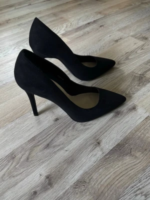 Svarta pumps - Stilrena svarta pumps från Nelly med spetsig tå och hög klack. Skorna är tillverkade i mockaimitation och har en klassisk siluett som passar till många olika tillfällen.