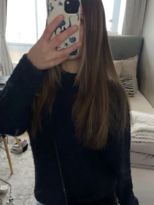 Mörkblå stickad tröja - Mysig mörkblå stickad tröja med rund hals och lång ärm. Tröjan har en avslappnad passform och är tillverkad i ett fluffigt, mjukt material som känns skönt mot huden. Perfekt att matcha med jeans för en enkel och snygg look.