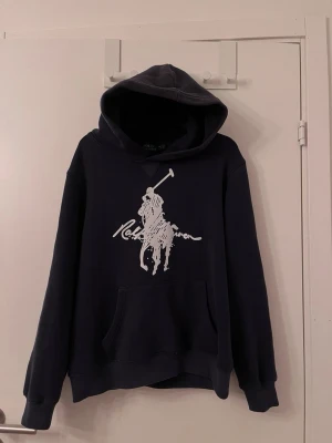 Ralph Lauren hoodie  - Tjena!! Jag säljer nu denna OTROLIGT snygga hoodie pga att den inte passar mig längre helt enkelt! Det är storlek M men den är liten i storleken så det är ungefär S nu, tror den krympt i tvätten🫣skicket är mycket bra bara 1 litet hål på baksidan under luvan som man ser på bild! Jag är rätt så säker på att den är äkta🤩säljer för endast 649kr, sett folk sälja för 900kr+💫va snabba, en väldigt sällsynt snygg hoodie! Hör av dig vid mer frågor eller funderingar! Mvh Ga