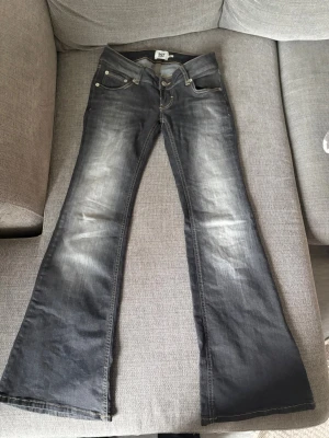 Grå bootcut jeans från 157 - Säljer ett par grå bootcut jeans från 157 med slitningar framtill för en cool vintage-look. Jeansen har klassisk femficksdesign, låg midja och kontrastsömmar. Perfekta för dig som gillar retrostil och vill sticka ut lite extra.