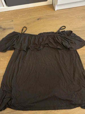 Svart offshoulder tröja från  Papaya - Säljer en svart offshoulder tröja  från Papaya med tunna axelband och volangdetalj upptill. Tröjan har en avslappnad passform och är perfekt för varma dagar. Enkel och stilren design som är lätt att matcha med jeans.
