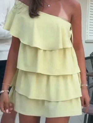  Populär Gul offshoulder volangklänning - Snygg gul kortklänning med flera volanger och offshoulder-design. Klänningen har en oneshoulder-skärning och är perfekt för varma dagar. Lätt och luftig känsla, passar dig som gillar trendiga och lekfulla plagg.