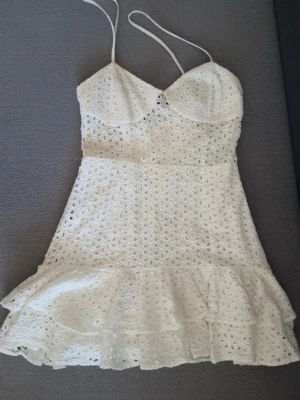  Ny Vit spetsklänning med volang - Söt vit kortklänning med tunna axelband och volangkant. Klänningen har ett broderat spetsmönster och en figurnära passform upptill. Perfekt för sommarens alla tillfällen och ger en romantisk vibe.