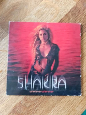 Shakira - Whenever Wherever singel - CD-singel med Shakira, 'Whenever Wherever'. Omslaget har en röd och svart ton med Shakira på framsidan och Machu Picchu i bakgrunden på baksidan. Innehåller låtarna 'Whenever, Wherever' och 'Suerte'. Perfekt för dig som gillar pop och samlar på musik från tidigt 2000-tal.