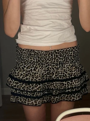Leopardmönstrad volangkjol - Säljer en kort kjol med leopardmönster och flera volanger. Kjolen har bred resår i midjan och svarta band som detaljer mellan volangerna. Perfekt för dig som vill sticka ut med en trendig look💕Den är i storleken 146/152 men den passar XS/S!