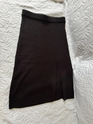 Svart ribbad kjol från NLY Trend - Säljer en svart ribbad långkjol från NLY Trend i mjukt stickat material. Kjolen har en slim passform och en snygg slits framtill som ger extra edge till din outfit. Perfekt att styla med en croppad topp eller oversized tröja.