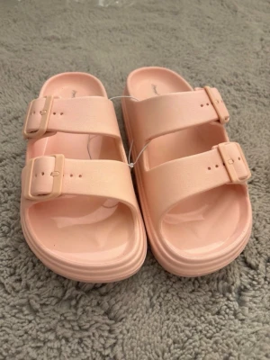 Ljusrosa sandaler från Happy Flops - Säljer ett par ljusrosa sandaler från Happy Flops med två breda remmar och justerbara spännen. Tillverkade i ett mjukt och flexibelt plastmaterial som är lätt att rengöra. Perfekta för chill dagar eller när du vill ha något bekvämt på fötterna. Dem är även ny köpta utan prislapp! pris kan diskuteras 