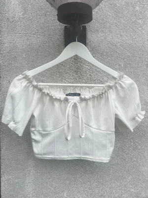 Vit off shoulder topp Boohoo - Söt vit off shoulder topp från Boohoo med puffärmar och rynkad kant upptill. Toppen har en dekorativ knytning framtill och är gjord i ett ribbat stretchigt material. 