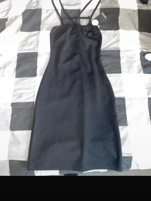 Svart tight klänning Boohoo - Snygg svart klänning från Boohoo med smala axelband och figurnära passform. Klänningen har en enkel, stilren design och är tillverkad i ett mjukt syntetmaterial. Perfekt för dig som gillar minimalistisk stil och vill ha en klassisk look.