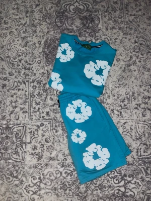 Turkost set med vita blommor - Säljer ett turkos sätt från denim tears, den är i nytt skick och är väldigt skönt att ha under sommaren. Det står att det är storlek L men det är fel i storleken. Den är skön att ha på sig. Priset är inte hucket i stenen.