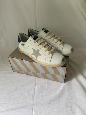 Golden goose vits sneakers  - Tja säljer ett par schyssta Golden goose men marin blå detalj och en sjärna som main detaljen. Dem är k skick 10/10. Inner sulan är 28,5 cm lång. 1499kr. Snabb affär 1299kr. Öppen för alla frågor. 