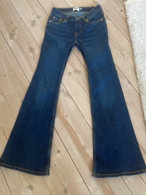 Blå utsvängda jeans från lager 157 - Säljer ett par blå jeans från lager 157 med utsvängda ben, klassisk femficksmodell och orangea kontrastsömmar. Modellen heter Bell och har en snygg retrovibe.