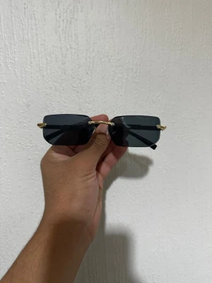 Cart1er glasögon  - Snygga solglasögon med rektangulära, svarta glas och tunna guldfärgade bågar. Glasen är mörka och utan synlig logga på framsidan. Perfekt accessoar för en trendig look.