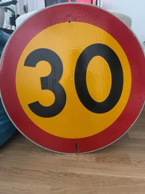 Rund hastighetsskylt 30 km/h - Stor rund hastighetsskylt i metall med gul botten, röd kant och svarta siffror. Skylten visar 30 km/h och är perfekt som dekoration eller samlarobjekt.             HÄMTAS PÅ PLATS 