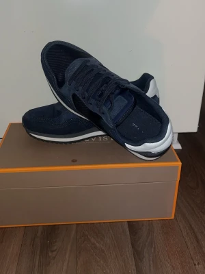 Mörkblå sneakers  - Snygga mörkblå sneakers med vit och svart sula. Ovandelen är i mesh och mockaliknande material, med klassisk snörning och låg profil. Perfekta för en sportig och stilren look.