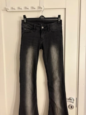 Svarta bootcut jeans från Cheap Monday - Säljer ett par svarta bootcut jeans från Cheap Monday med snyggt slitna detaljer framtill och baktill. Jeansen har klassisk femficksmodell, normal midja och lila Cheap Monday-märke bak. Perfekta för dig som gillar en avslappnad men trendig look.