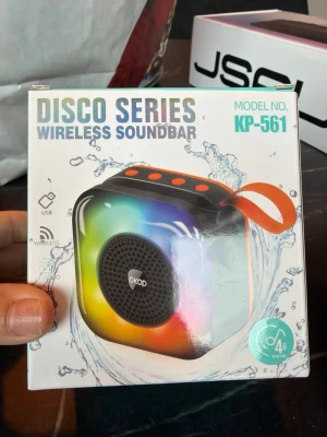 Disco Series trådlös högtalare KP-561 - Färgglad och kompakt trådlös högtalare från OKOD, modell KP-561. Högtalaren har LED-belysning i regnbågens färger, svart front med rund högtalargaller och orange bärrem. Utrustad med USB och trådlös anslutning. Perfekt för att ta med överallt.