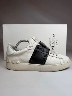 Valentino Garavani opens - Snygga vita sneakers från Valentino Garavani med svart läderdetalj och ikoniska nitar över vristen. Skorna har snörning och en chunky sula med nitar längs hälen. Perfekta för dig som gillar exklusiv streetstyle.