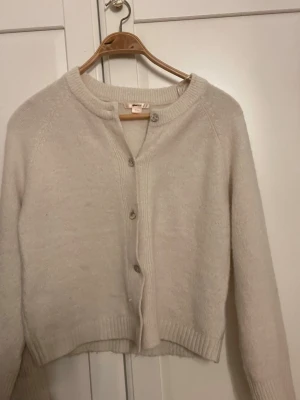 Krämvit kofta från Gina Tricot - Mysig krämvit kofta från Gina Tricot med rund halsringning och knappar frammtill är använd men knappt tecken på det 