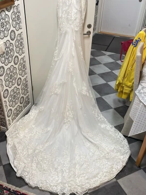 Brudklänning - Drömmig vit brudklänning från milla nova, inköpt för 20.000kr med djup v-ringning och tunna axelband. Klänningen har vackra broderade spetsdetaljer och blommigt mönster över hela tyget. Perfekt för dig som vill ha en romantisk och elegant look. Säljes billigt då jag verkligen vill bli av med den