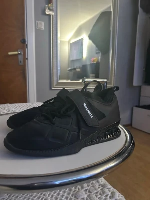 Svarta sneakers från MM Sports - Snygga helsvarta sneakers från MM Sports med modern design. Skorna har en låg silhuett, snörning och kardborreband för extra support. Ovandelen är i syntetmaterial och sulan har en cool struktur. Perfekta för dig som gillar sportig och stilren look.