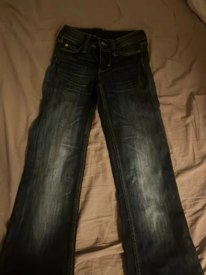 Mörkblå bootcut jeans med patch - Snygga mörkblå bootcut jeans med slitningar och kontrastsömmar. Baktill finns en orange patch med tryck på linningen. Jeansen har klassisk femficksdesign och är tillverkade i denim. Dom är ifrån weekday/cheap monday, väldigt töjbara, storlek 23 men passar 24.