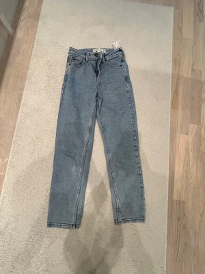Ljusblå raka jeans från Stradivarius - Säljer ett par oanvända ljusblå jeans från Stradivarius i rak modell. Klassisk femficksdesign, hög midja och bälteshällor. Jeansen är tillverkade i bomull och har en avslappnad vintagekänsla. Perfekta till en casual look och enkla att styla med sneakers eller boots.