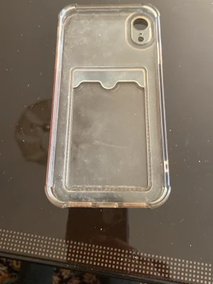 Transparent mobilskal med kortfack - Säljer ett genomskinligt mobilskal med inbyggt kortfack på baksidan. Skalets kanter är förstärkta för extra skydd och det är gjort av flexibel plast. Passar en mobil med kamera i övre vänstra hörnet. Perfekt för dig som vill ha både skydd och plats för kort.