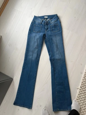 Blå bootcut jeans med fickor från madlady - Säljer ett par blå bootcut jeans från Madlady med markerade sömmar framtill och två stora fickor fram. Jeansen har hög midja och klassisk femficksdesign. Perfekta för en trendig och avslappnad look.