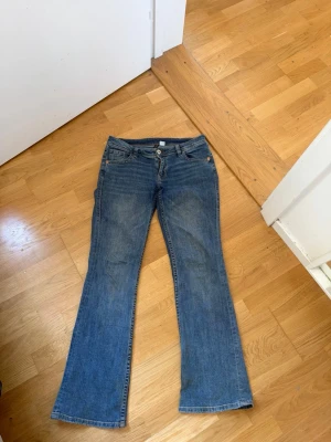 Blå bootcut jeans med slitning - Ett par klassiska blå bootcut jeans i denim med låg midja. Jeansen har en snygg tvätt och slitningar vid benslutet . 