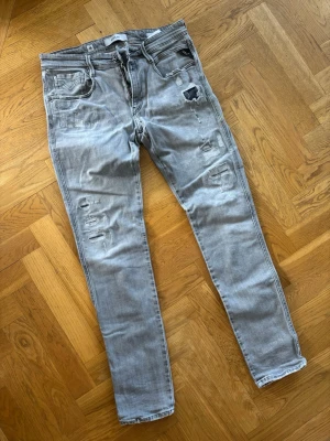 Replay anbass slitna - Säljer ett par grå jeans från Replay jeans med slim fit och slitningar på benen för en trendig look. Jeansen har klassisk femficksmodell, läderpatch bak och är tillverkade i mjuk denim. Perfekta för dig som gillar en avslappnad men stilsäker stil.