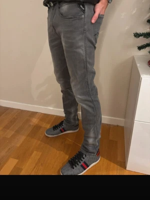 Replay Anbass - Säljer ett par gråa slim fit jeans från Replay med snygga slitningar och klassiska femficksdetaljer. Jeansen har en modern passform och är tillverkade i mjukt denim-material som ger en skön känsla. Perfekta för dig som gillar en stilren look.
