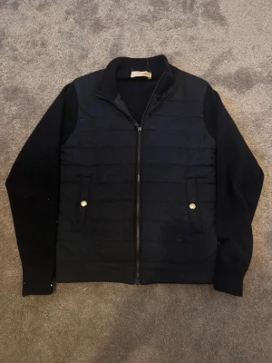 Sayless Cardigan - Snygg svart tröja med vadderad framsida och stickade ärmar. Tröjan har hel dragkedja, ståkrage och två fickor framtill med knappdetaljer. Perfekt för lager-på-lager och en clean look.                       Storlek: XS                                                                Skick: 9/10                                                                   Frakt: inom 24h