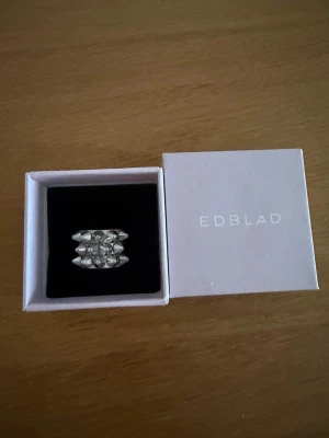Edblad silvrig ring med pärldetaljer - Cool och bred ring från Edblad i silverfärg med flera små pärlliknande detaljer i ett geometriskt mönster. Ringen har en modern och edgy design som verkligen sticker ut. Levereras i original ask.