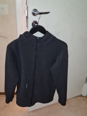 Mörkgrå zip hoodie - Mörkgrå hoodie med dragkedja framtill och huva. Klassisk modell med långa ärmar och ribbade muddar. Perfekt för en avslappnad och enkel stil. Materialet känns mjukt och bekvämt, troligen bomullsblandning.