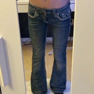 Rock Revival bootcut jeans - Jeans från Rock Revival med låg midja. Jeansen har tydliga kontrastsömmar, snygga broderier, detaljer på fickorna och en unik wash. Materialet är klassisk denim och passformen är bootcut. Midja: 39cm rakt över. Innerben: 80cm. |Beskrivningen överst & de tre första bilderna är från förra ägaren. 💕Några stenar på framfickan har åkt av i tvätten(bild 5). Liten defekt på höger lår (bild6)Köpta för 900kr💕Säljer då dem inte blir använda💕